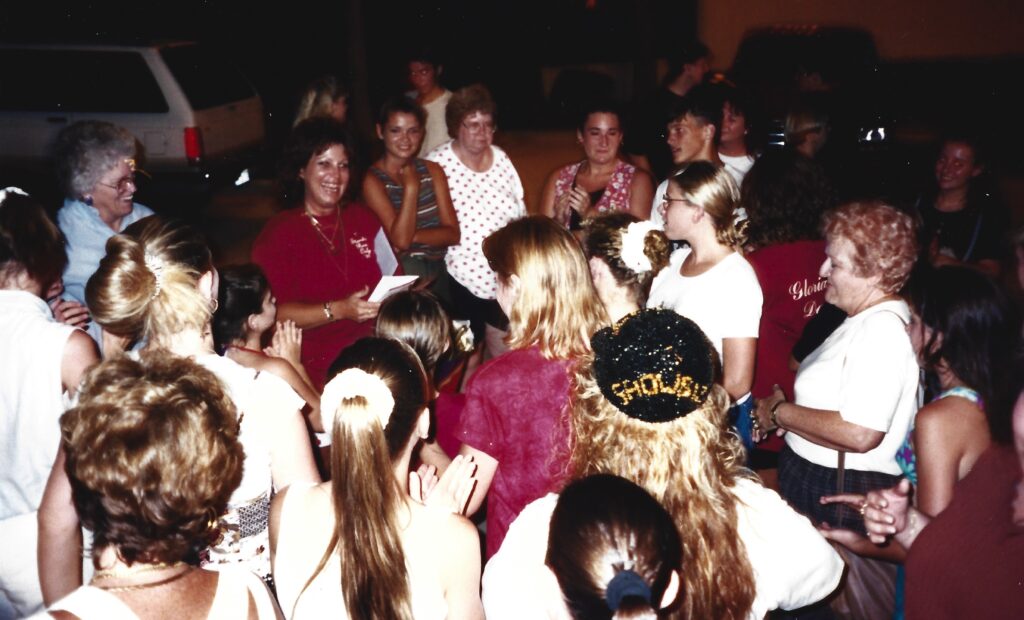 A group of people all surrounding a smiling woman with dark hair wearing a maroon shirt. 