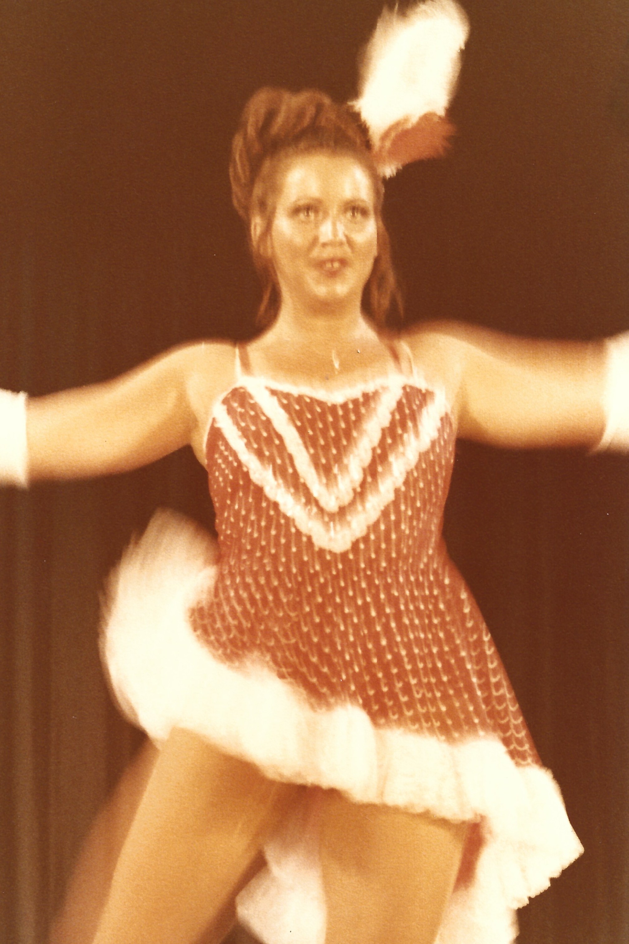 A somewhat blurred image of a dancer wearing a white feather and a red costume with white trim and polka dots. 