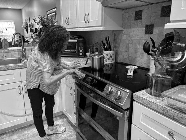 Woman in kitchen turning up heat on oven.