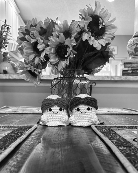 Two crocheted ghosts on dining room table in front of bouquet of sunflowers.