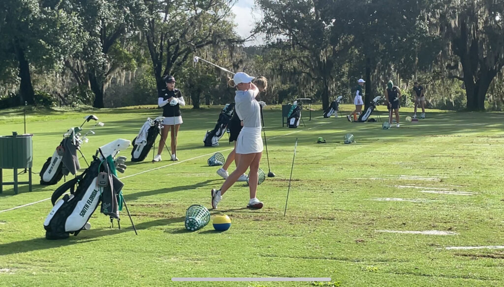 A golfer takes a swing while at the driving range and looks while the ball soars away.