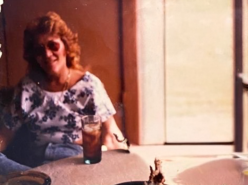 A woman sits at a kitchen table in an old looking snapshot