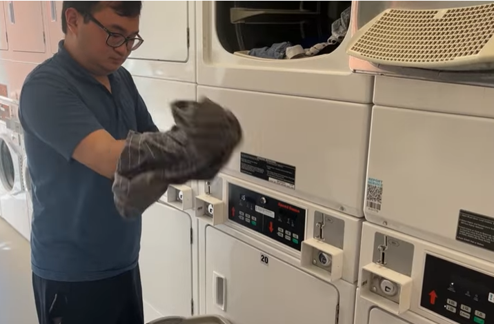A student pulls a shirt inside out in front of an open washing machine