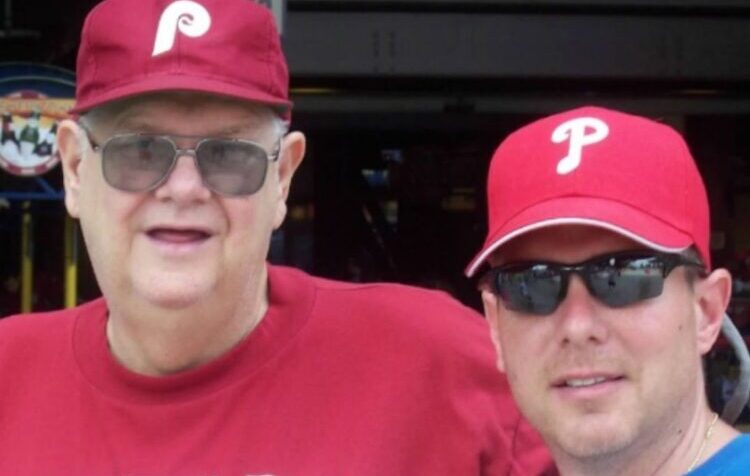 Two men in Philadelphia Phillies shirts and hats attend a baseball game