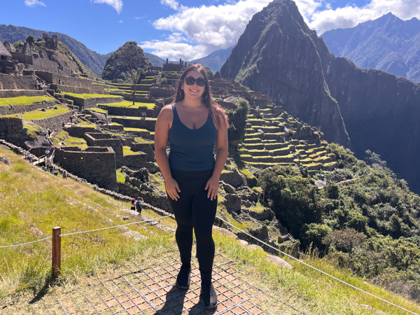 A woman stands along a mountain ridge with terraces in Macchu Picchu