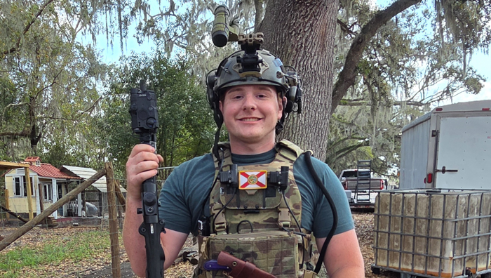 A man dressed in camo and a night vision helmet holds a rifle