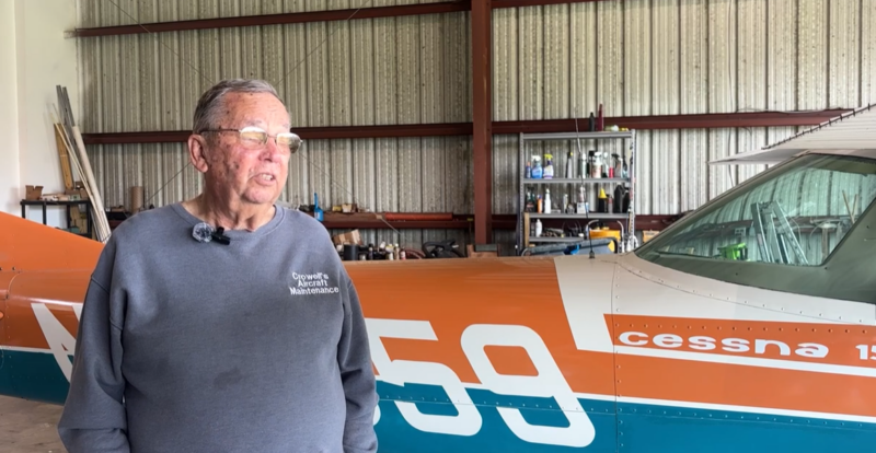 A man stands in front an an orange and blue Cessna airplane