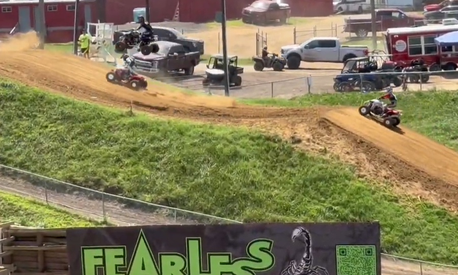 Four wheel racers fly and race along a dirt track