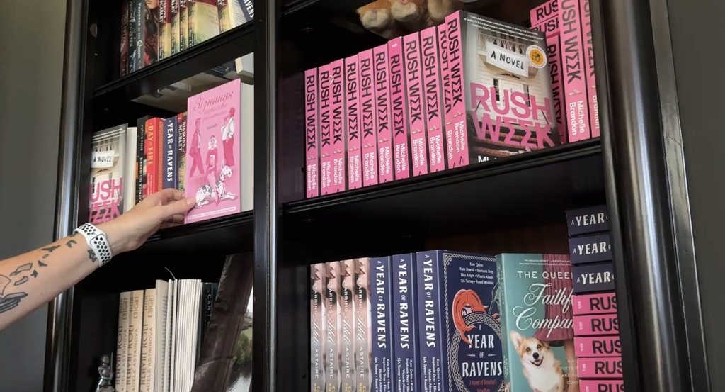 Eliza Knight reaching for one of her novels on her bookshelf filled with her newest releases.