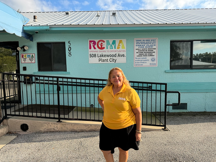 Maria Estrella stands smiling outside the RCMA center in Plant City, wearing a yellow RCMA shirt and black pants.