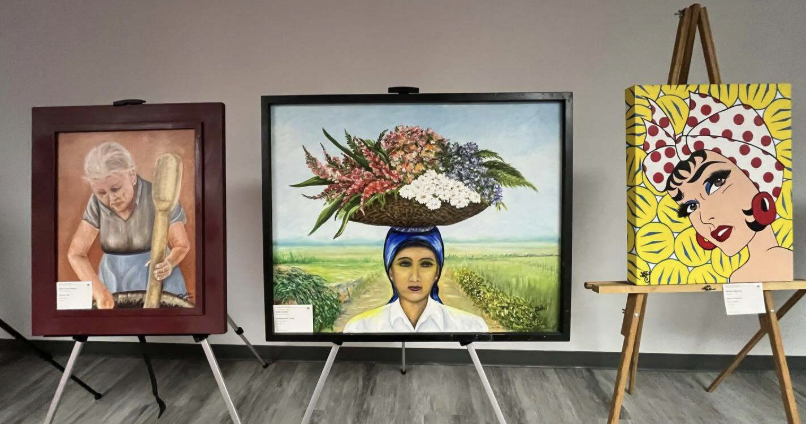 This is a photo of three paintings at an art show. The first painting on the left shows an older woman mixing something in a bowl. The woman in the middle has flowers in a bowl on top her head. While the third woman has a red and white scarf on her head amongst a yellow background.