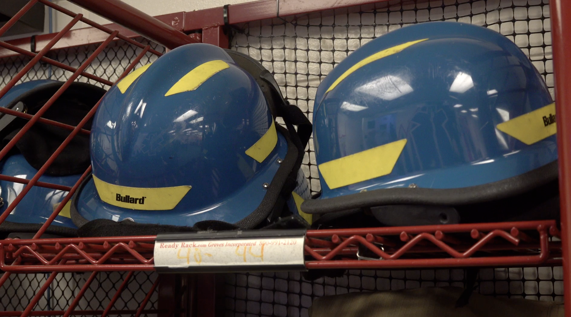 These are two blue hard hats sitting on top of a red shelf