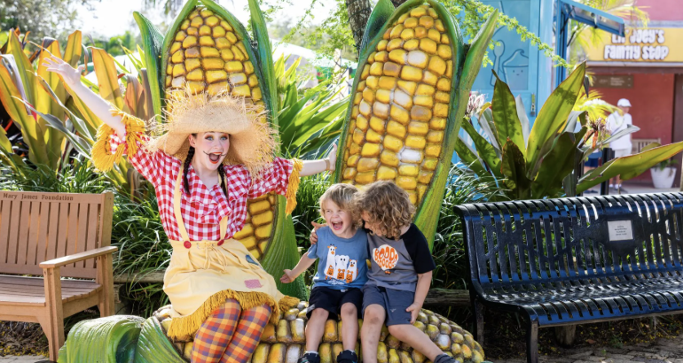 This image shows two kids sitting with a scarecrow on a corn bench